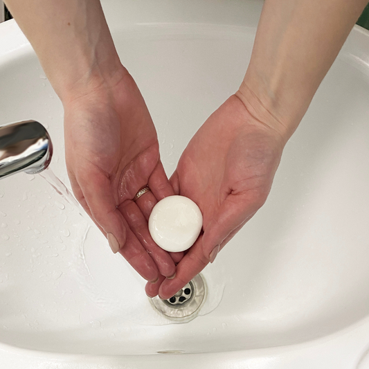 Person holding a small white soap medallion under running water in the sink