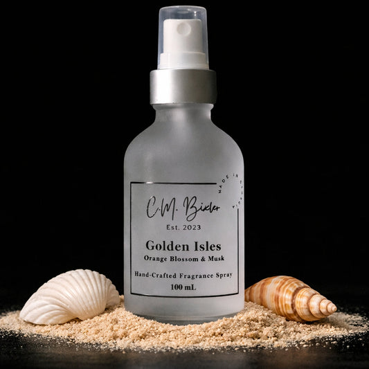 Fragrance spray bottle labeled 'Golden Isles' with seashells on sand against a black background